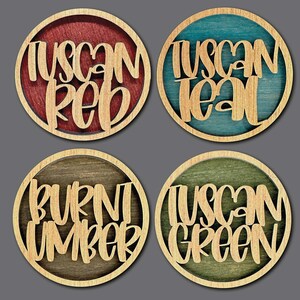 Może przedstawiać: Cztery drewniane podkładki pod kubki z r&oacute;żnymi plamami kolorystycznymi i tekstem. Podkładki mają napis "Tuscan Red", "Tuscan Teal", "Burnt Umber" i "Tuscan Green".