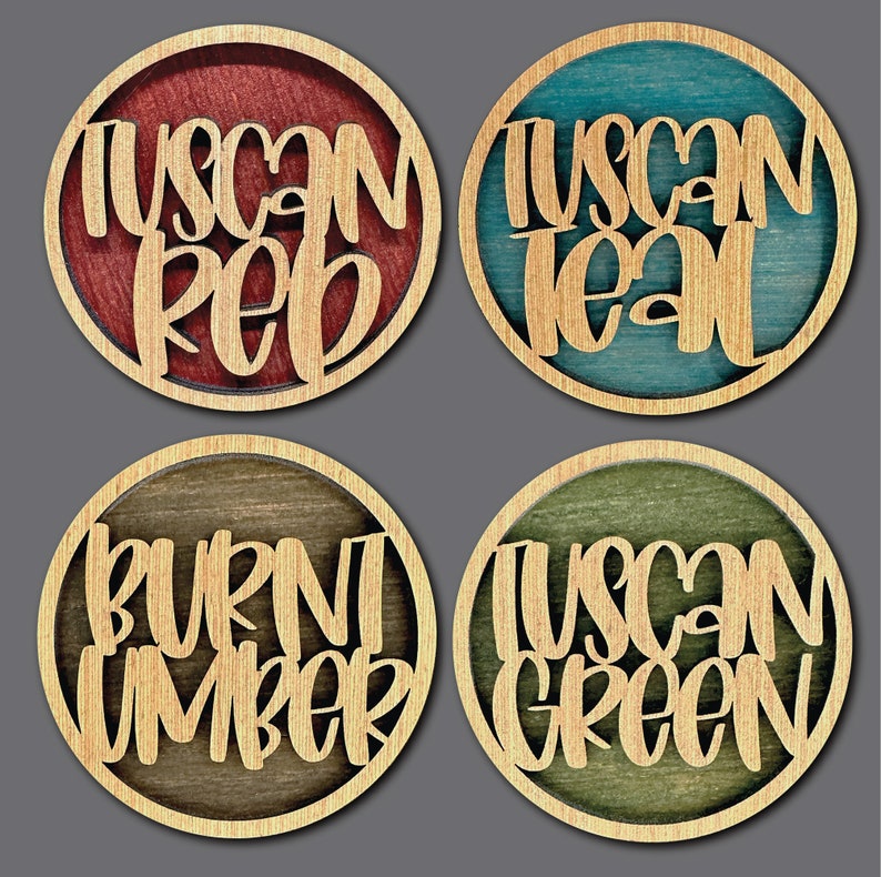 Może przedstawiać: Cztery drewniane podkładki pod kubki z r&oacute;żnymi plamami kolorystycznymi i tekstem. Podkładki mają napis "Tuscan Red", "Tuscan Teal", "Burnt Umber" i "Tuscan Green".