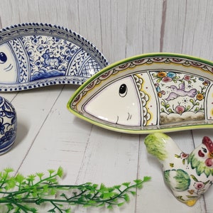 Pode incluir: Pratos de cerâmica e saleiros e pimenteiros com tema de peixe e galinha. Os pratos em forma de peixe são brancos com padrões florais azuis e desenhos coloridos. Os saleiros e pimenteiros são azuis e brancos com padrões florais.