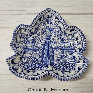 May include: A blue and white ceramic dish shaped like a leaf with a floral design and two rabbits. The dish is decorated with a blue and white floral pattern and has a scalloped edge.