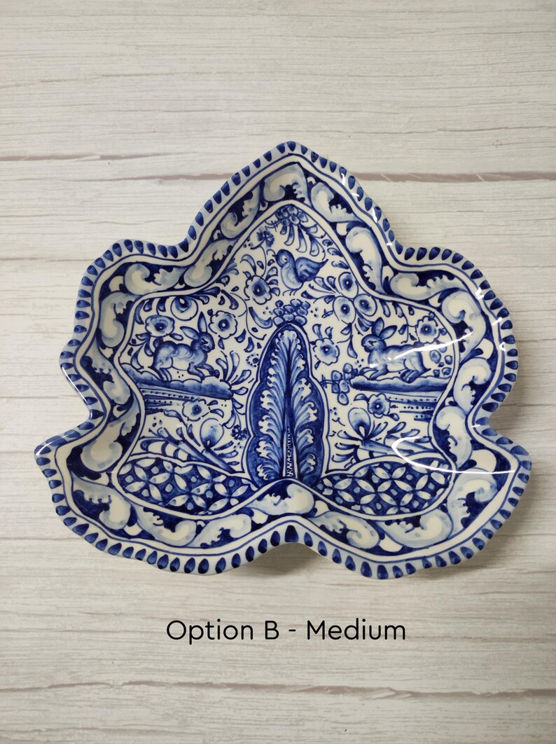 May include: A blue and white ceramic dish shaped like a leaf with a floral design and two rabbits. The dish is decorated with a blue and white floral pattern and has a scalloped edge.