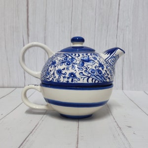 Peut inclure: Service à thé individuel en céramique blanche et bleue. La théière présente un motif floral bleu et un couvercle assorti. La tasse à thé a des rayures bleues. L'ensemble est conçu pour une personne.