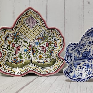 May include: Two ceramic serving dishes shaped like leaves. The larger dish is decorated with a floral pattern in shades of pink, yellow, green, and blue. The smaller dish is decorated with a blue and white floral pattern.