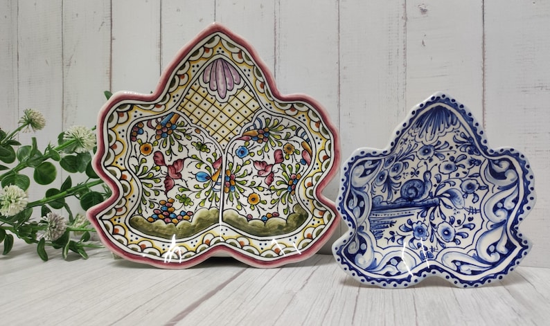 May include: Two ceramic serving dishes shaped like leaves. The larger dish is decorated with a floral pattern in shades of pink, yellow, green, and blue. The smaller dish is decorated with a blue and white floral pattern.