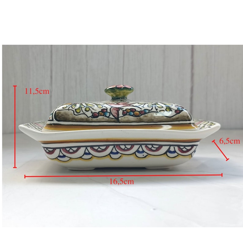 Puede incluir: Un mantequillero de cer&aacute;mica con tapa, que presenta un dise&ntilde;o floral colorido en tonos de verde, rojo, amarillo y azul. El plato mide 6,5 cm de ancho, 11,5 cm de alto y 16,5 cm de largo.