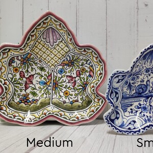May include: Two ceramic leaf-shaped serving dishes, one medium and one small. The medium dish is yellow with green, red, and blue floral designs. The small dish is blue and white with a floral design.