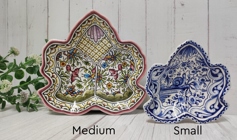 May include: Two ceramic leaf-shaped serving dishes, one medium and one small. The medium dish is yellow with green, red, and blue floral designs. The small dish is blue and white with a floral design.