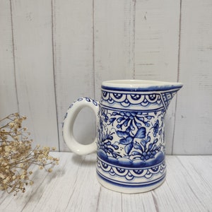 May include: A white ceramic jug with a blue and white floral pattern. The jug has a handle and a spout.