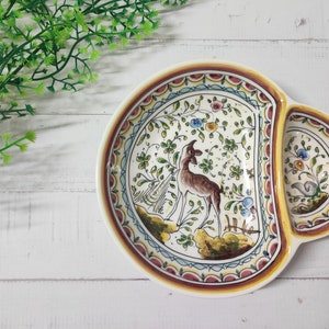 May include: A white ceramic serving dish with a divided section. The dish is decorated with a colorful floral pattern and a deer in the center. The rim of the dish is trimmed in red, yellow, and blue.