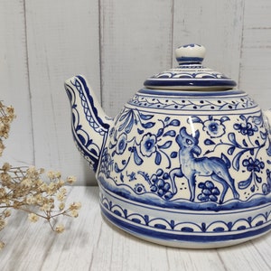 Pode incluir: Uma chaleira de cerâmica azul e branca com um design floral e animal. A chaleira tem um corpo redondo e um bico no lado. A alça está no lado direito da chaleira. A tampa tem uma pega no topo.