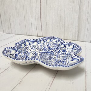 May include: A white ceramic serving dish with a blue and white floral pattern. The dish has a scalloped edge and a unique, irregular shape.