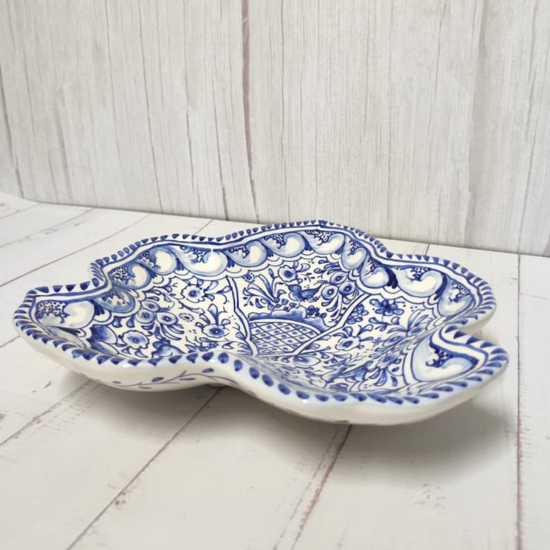 May include: A white ceramic serving dish with a blue and white floral pattern. The dish has a scalloped edge and a unique, irregular shape.