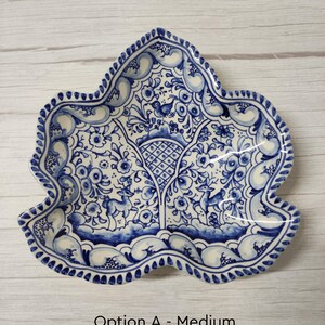 May include: A blue and white ceramic dish with a leaf shape and intricate floral designs. The dish features a bird and deer in the center.
