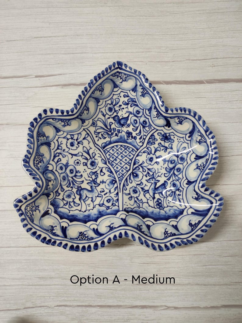 May include: A blue and white ceramic dish with a leaf shape and intricate floral designs. The dish features a bird and deer in the center.