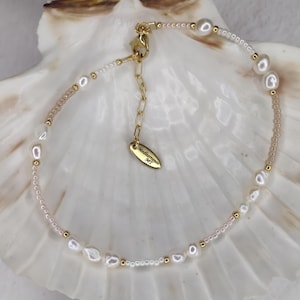 May include: A delicate gold bracelet with freshwater pearls and small gold beads. The bracelet has a lobster clasp and an adjustable chain. A small gold tag reads "Mediterraneo MT". The bracelet is displayed on a white seashell.