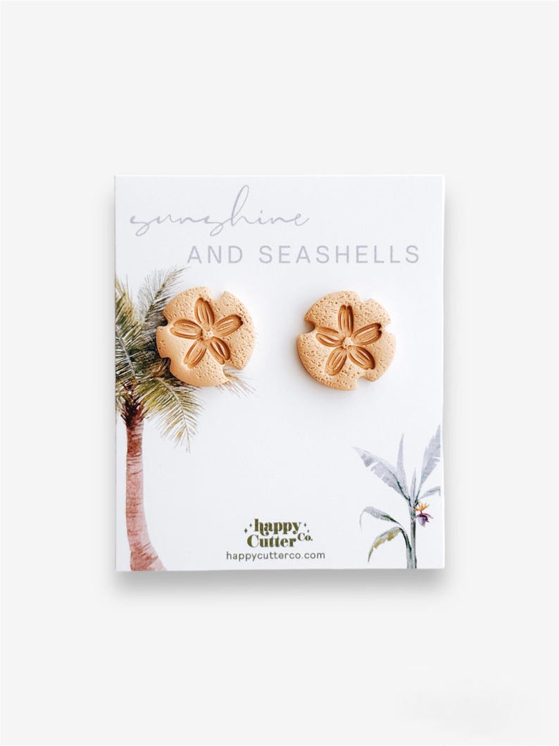 A pair of handmade white sand dollar stud earrings crafted from lightweight polymer clay, displayed on a beachy card featuring a simple palm tree illustration and the phrase “Sunshine and Seashells.” A coastal-inspired summer accessory, perfect for beach lovers and ocean vibes.