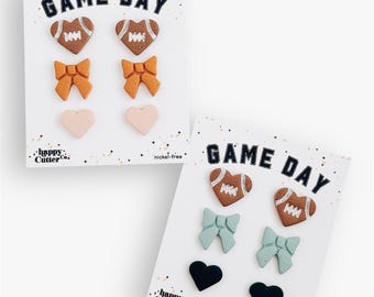 Könnte beinhalten: Zwei Karten mit dekorativen Formen. Auf jeder Karte steht oben "GAME DAY". Eine Karte hat herzförmige Fußbälle, orangefarbene Schleifen und rosa Herzen. Die andere Karte hat herzförmige Fußbälle, blaue Schleifen und schwarze Herzen.