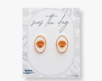 Könnte beinhalten: Ein Paar goldfarbene Muschel-Ohrstecker auf einer weißen Karte mit dem Text "Seas the day" und "Happy Cutter Co." Die Karte trägt außerdem den Hinweis "nickel free".