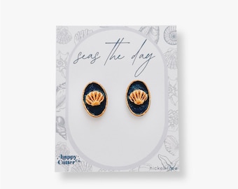 Könnte beinhalten: Ein Paar goldene und blaue Muschel-Ohrstecker auf einer weißen Karte mit dem Text "Seas the day" und "Happy Cutter Co." und "nickel free".