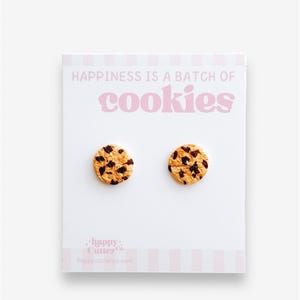 May include: A pair of small, round, chocolate chip cookie earrings. The earrings are on a white card with the text "Happiness is a batch of cookies" and the logo "Happy Cutter Co."