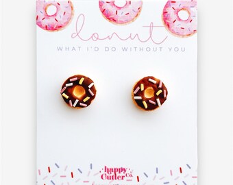 Könnte beinhalten: Ein Paar Donut-förmige Ohrstecker mit Schokoladenüberzug und rosa, gelben und violetten Streuseln. Die Ohrringe werden auf einer weißen Karte mit dem Text "donut what I'd do without you" und einem rosa-weißen Streuselmuster präsentiert.