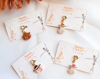 Könnte beinhalten: Vier Halloween-Anhänger auf Karten. Die Anhänger zeigen einen Kürbis, einen Geist und eine Hexe, jeweils mit einem goldfarbenen Verschluss. Die Karten tragen den Text "happy Cutter Co. CHARM" und eine Skelettgrafik.