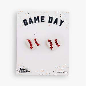 Könnte beinhalten: Weiße herzförmige Ohrringe mit roten Nähten, die Basebällen ähneln, auf einer weißen Karte präsentiert. Die Karte zeigt den Text "GAME DAY" in Marineblau und den Markennamen "happy cutter co."