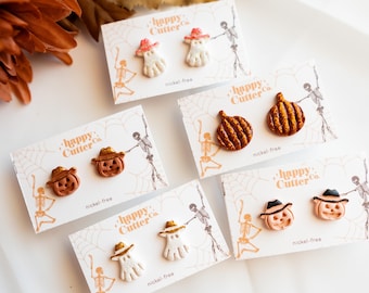 Könnte beinhalten: Eine Auswahl an Halloween-Ohrringen. Die Ohrringe zeigen Geister, Kürbisse und Jack-o'-Laternen, jeweils mit Hut. Die Ohrringe sind auf Karten mit dem Text "happy Cutter Co." und "nickel-free" präsentiert.