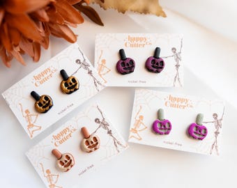 Könnte beinhalten: Ohrstecker im Halloween-Design in Kürbisform. Die Ohrringe sind in Gold, Lila und Beige erhältlich und werden auf Karten mit der Aufschrift "happy Cutter Co." und "nickel-free" präsentiert.