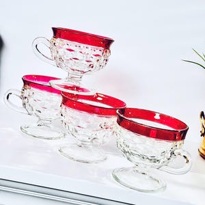 May include: Set of four clear glass cups with a red rim. The cups have a diamond pattern and a pedestal base.