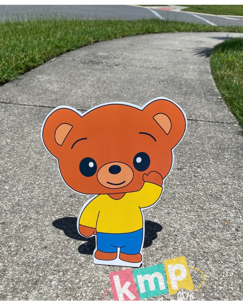 Puede incluir: Un personaje de dibujos animados de oso marr&oacute;n con una camisa amarilla y pantalones azules est&aacute; saludando. El personaje est&aacute; de pie en una acera gris.