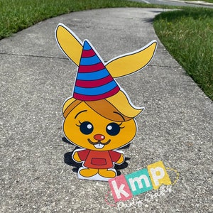 Puede incluir: Un personaje de dibujos animados amarillo con un gorro de fiesta rojo y azul, que lleva un vestido rojo con un cuello amarillo y un delantal blanco. El personaje tiene una nariz amarilla, ojos marrones y un peque&ntilde;o bigote. El personaje est&aacute; de pie en una acera gris. El texto "kmp Party Crafts" es visible en la esquina inferior derecha de la imagen.