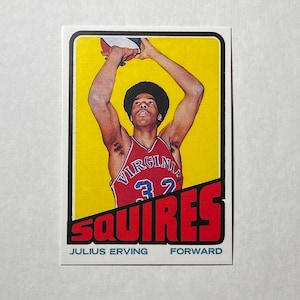 May include: Vintage basketball trading card featuring Julius Erving of the Virginia Squires. The card has a yellow background with a red and white design. Erving is shown in a red jersey with the number 32, mid-shot with the basketball.