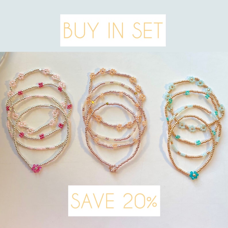 May include: Set of three beaded bracelets with flower charms. The bracelets are in pink, peach, and teal colours. The text "BUY IN SET SAVE 20%" is displayed above the bracelets.