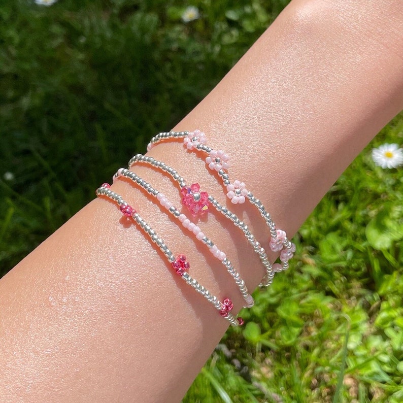 May include: A set of four beaded bracelets with pink and silver beads. The bracelets feature small pink flower charms.