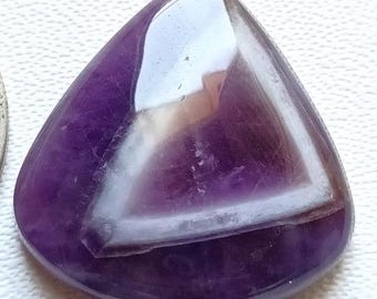 May include: A polished, triangular amethyst gemstone with a white band, next to a U.S. quarter. The gemstone is a deep purple color with a glossy finish. The quarter is silver and shows the profile of George Washington.