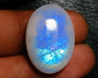 Può includere: Pietra preziosa a forma ovale di pietra di luna iridescente. La pietra mostra una base bianca lattea con riflessi interni blu e turchese. La superficie lucida riflette la luce, mostrando un gioco di colori. Una gemma per la creazione di gioielli.