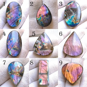 May include: Nine polished labradorite gemstones in various shapes, including oval, teardrop, and rectangular. The stones display iridescent flashes of blue, purple, and gold. Each gemstone is unique, showcasing natural patterns and colors.