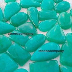 May include: A collection of polished, turquoise-colored gemstones in various shapes, including teardrop, oval, and rectangular. The stones have a smooth, glossy finish. The text "stonescompany" is visible on some of the stones.