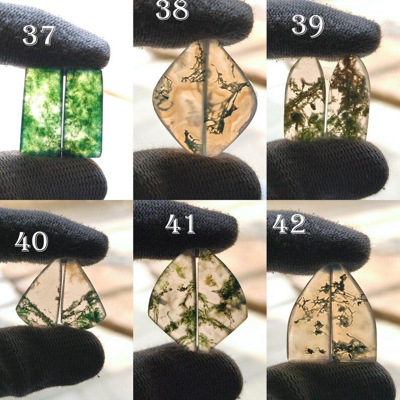 May include: A collection of six pairs of polished gemstone cabochons, each held by a gloved hand. The stones display a variety of colors, including green, brown, and clear, with unique internal patterns. The shapes vary from rectangular to diamond and teardrop.