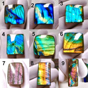 May include: A collection of nine polished labradorite gemstones labeled one through nine, displaying iridescent flashes of blue, green, yellow, and pink. Each stone features a smooth, reflective surface with natural internal fractures and color variations.