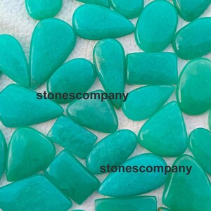 May include: A collection of polished, turquoise-colored gemstones in various shapes, including teardrops, rectangles, and ovals. The gemstones are scattered across a white surface, with the text "stonescompany" visible on some of them.