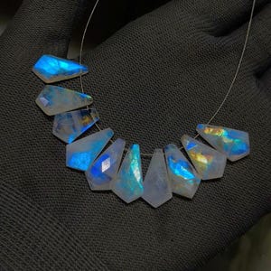 May include: A strand of iridescent moonstone beads. Each bead is a unique, faceted shape, displaying flashes of blue, yellow, and white. The beads are strung on a thin, silver-colored wire, creating a necklace-like arrangement.
