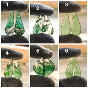 May include: Six pairs of moss agate gemstone cabochons are displayed, each held by a gloved hand. The cabochons feature green, white, and clear patterns. The gemstones are teardrop and diamond shaped. The image showcases the variety of the stones.