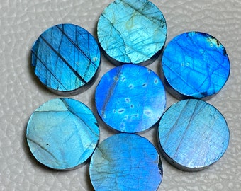 May include: Seven round, polished labradorite gemstones. Each stone displays a vibrant play of blue and teal colors with unique internal patterns. The stones are arranged in a circular pattern, showcasing their iridescent qualities.