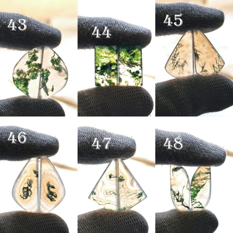 May include: A collection of six polished moss agate gemstone pairs, each with unique patterns of green moss-like inclusions. The stones are held by a gloved hand, showcasing their translucent quality and varied shapes, including teardrop, rectangular, and triangular forms.