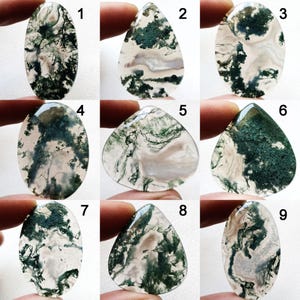 Puede incluir: Nueve piedras preciosas de ágata musgosa pulidas en varias formas, incluyendo ovaladas y de lágrima. Las piedras presentan fondos blancos y grises translúcidos con intrincadas inclusiones verdes, parecidas al musgo. Cada piedra se sostiene entre los dedos.