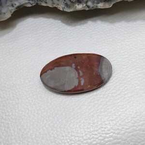 May include: Oval-shaped polished stone with a mix of colours. The stone features a blend of reddish-brown, grey, and white hues. The polished surface has a smooth texture, with a natural pattern. The stone is a decorative item.