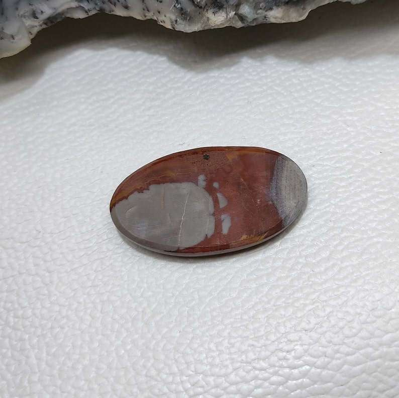 May include: Oval-shaped polished stone with a mix of colours. The stone features a blend of reddish-brown, grey, and white hues. The polished surface has a smooth texture, with a natural pattern. The stone is a decorative item.
