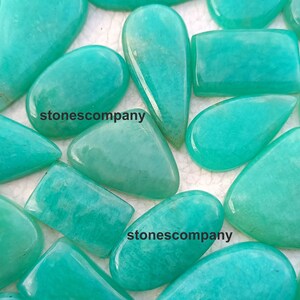 May include: A collection of polished amazonite gemstones in various shapes, including ovals, teardrops, and rectangles. The stones are a vibrant turquoise color with a smooth, glossy finish. The text "stonescompany" is visible on some stones.